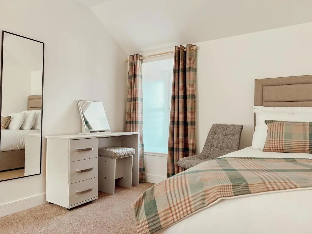 a bedroom with a bed and a mirror and a chair at Loch Ness Gatehouse Apartments in Fort Augustus
