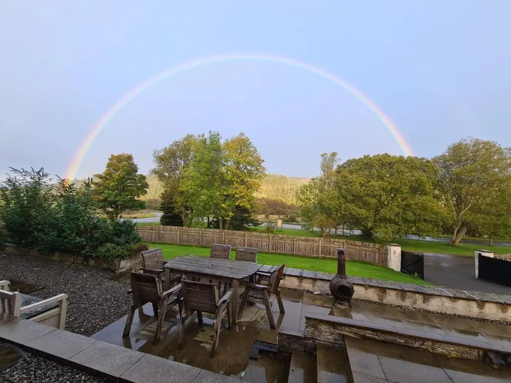 a table and chairs with a rainbow in the background at Cosy Spacious Highland Cottage in Craggie