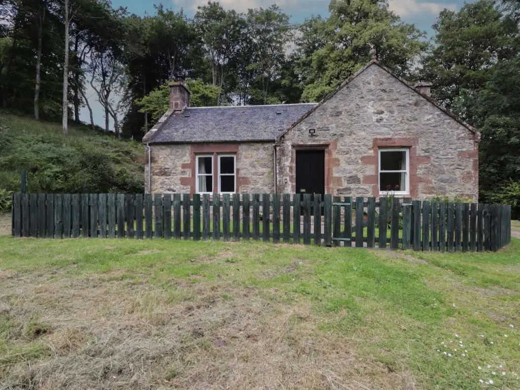 an old stone house with a wooden fence at Gunroom Cottage in Strathpeffer