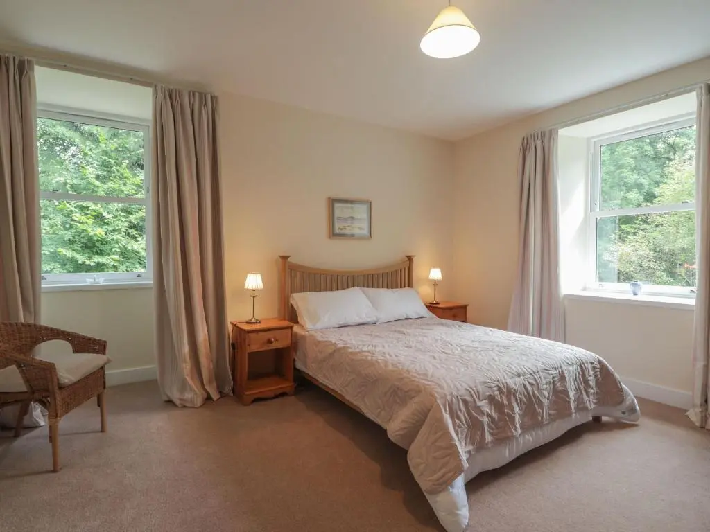 a bedroom with a bed and two windows at Gunroom Cottage in Strathpeffer