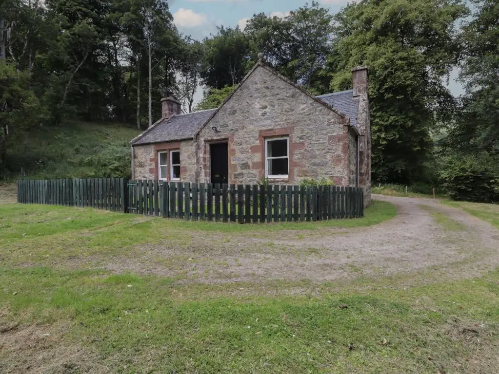 an old stone house with a fence in a field at Gunroom Cottage in Strathpeffer