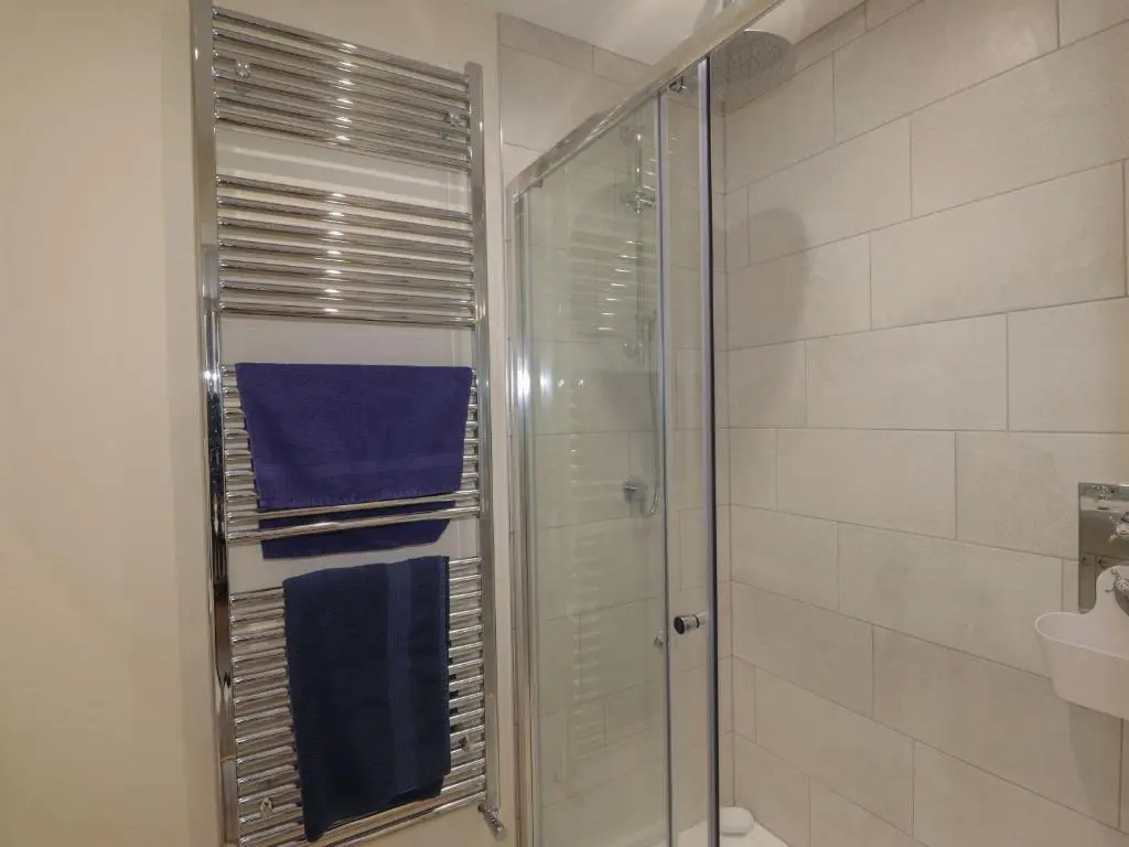 a bathroom with a glass shower with blue towels at Gunroom Cottage in Strathpeffer