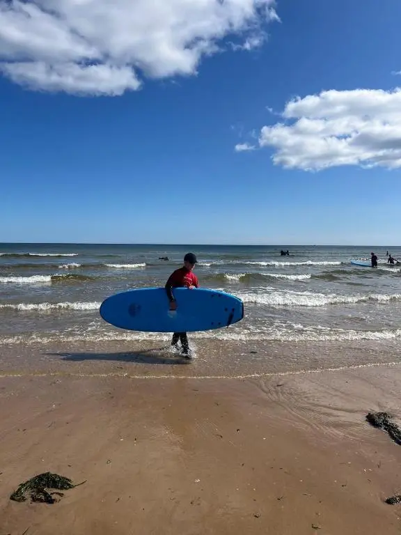 a man holding a blue surfboard on the beach at The Annexe in Lossiemouth