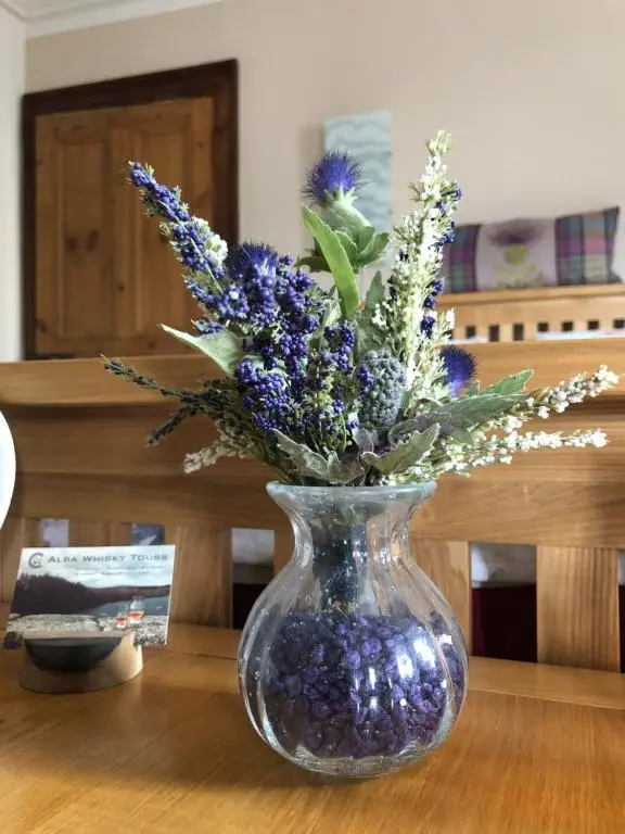 a glass vase with purple flowers in it on a table at Haus Alba in Grantown on Spey