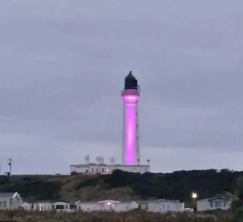 a lighthouse is lit up in pink at night at Lewis Sands PC114 in Lossiemouth