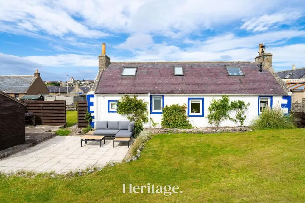 a white house with a bench in a yard at Beach Cottage, Pet & Family Friendly Stay in Moray in Lossiemouth