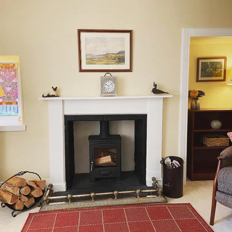 a living room with a fireplace with a clock on top at Dalvey Mill Cottage in Forres
