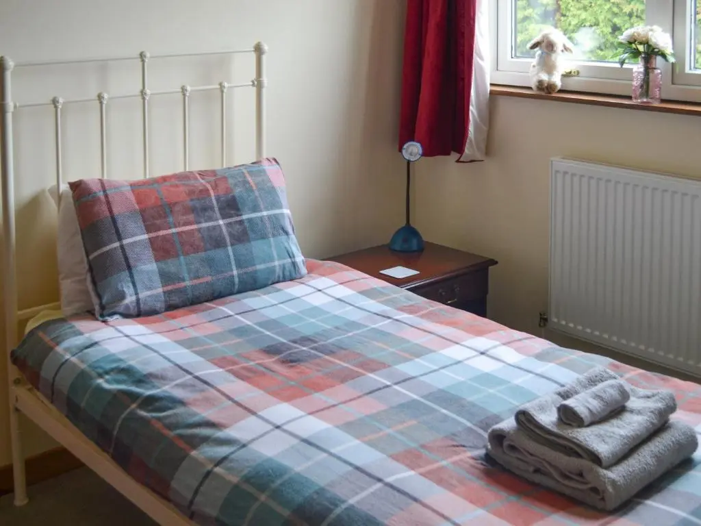 a bed with a blanket and two towels on it at The Junipers in Tain