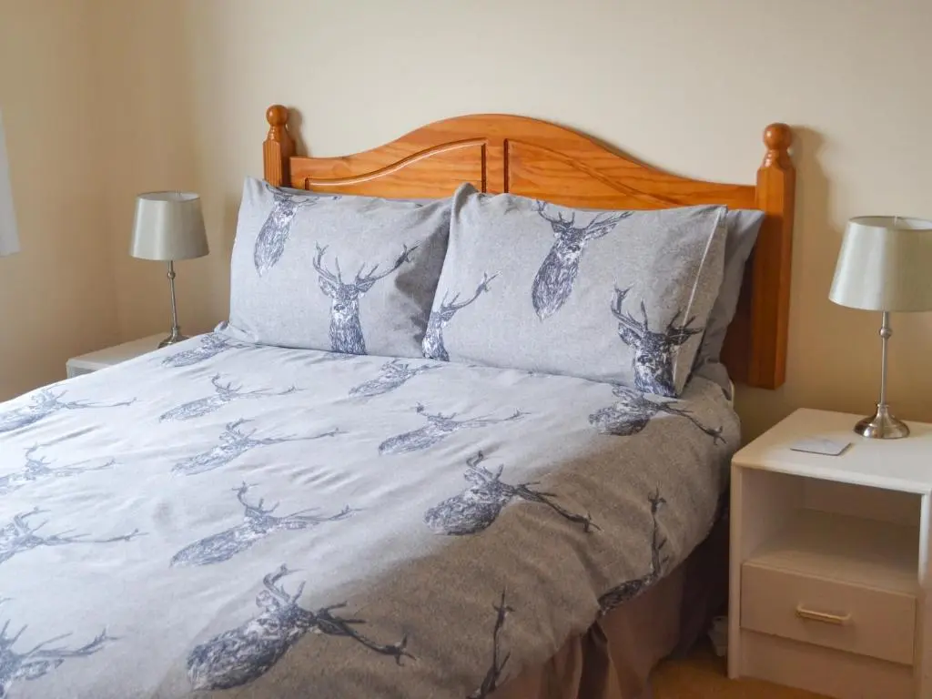 a bed with a blue and white comforter and two lamps at The Junipers in Tain