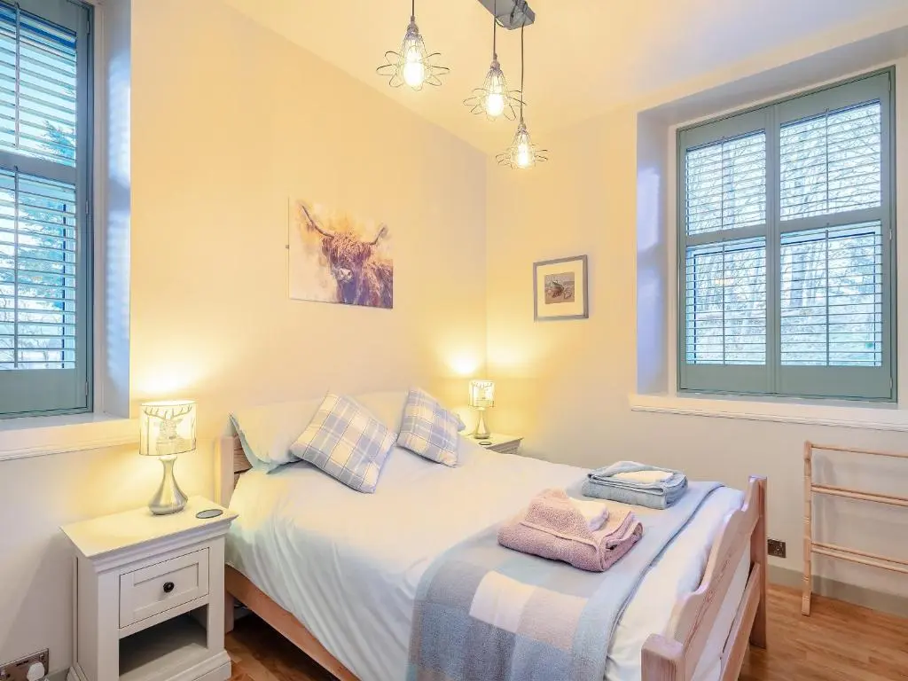 a bedroom with two beds and two windows at Rowan Cottage in Huntly