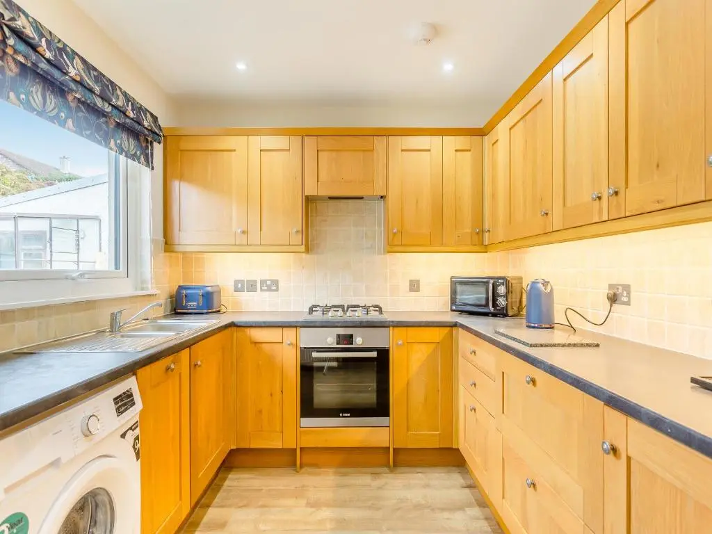 a kitchen with wooden cabinets and a washer and dryer at Mermaid View in Balintore