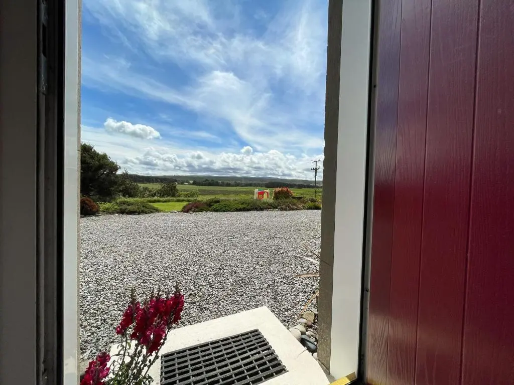 an open door with a view of a gravel road at Pine Cottage - Dalcross in Dalcross