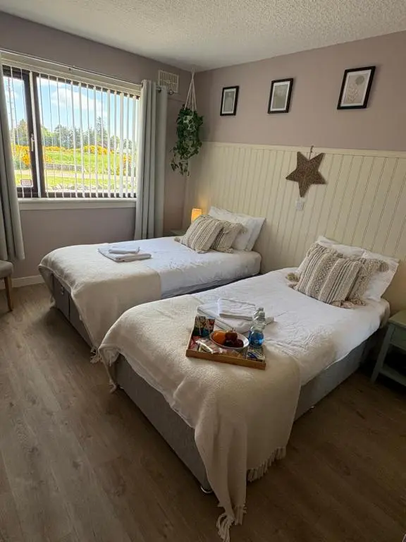 two beds in a bedroom with a tray of food at Carnegie Lodgings, Tain in Tain