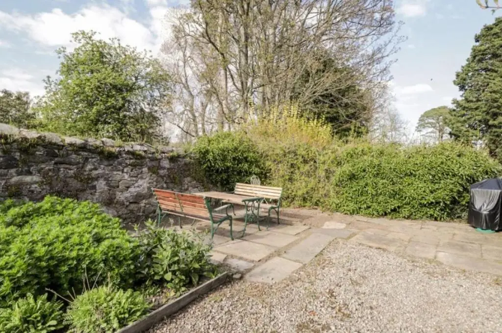 a table and benches in a garden with a stone wall at The Garden Flat - Ardullie Lodge in Dingwall