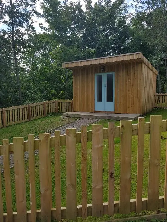 a small wooden building behind a fence at BCC Lochness Hostel pods in Bearnock