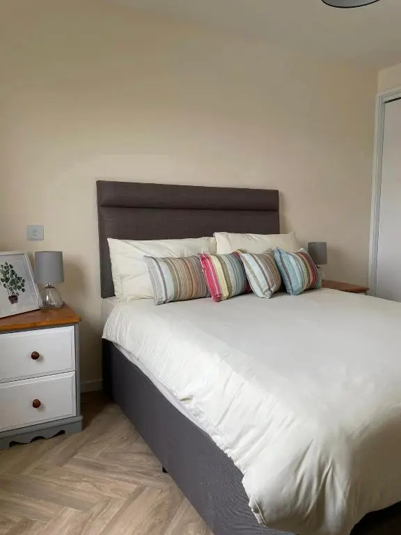 a bedroom with a white bed with pillows and a night stand at Wick Bay Apartments in Wick
