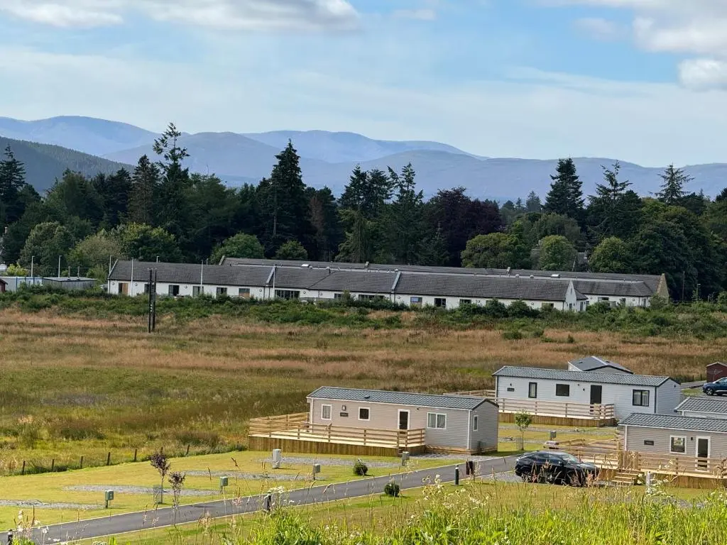 a group of buildings in a field with mountains in the background at Wildcat Lodge Grantown on Spey in Grantown on Spey