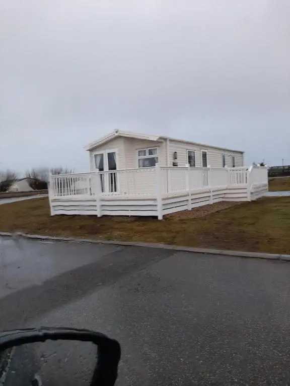 a white house with a porch and white fence at Swallows at Silversands in Lossiemouth