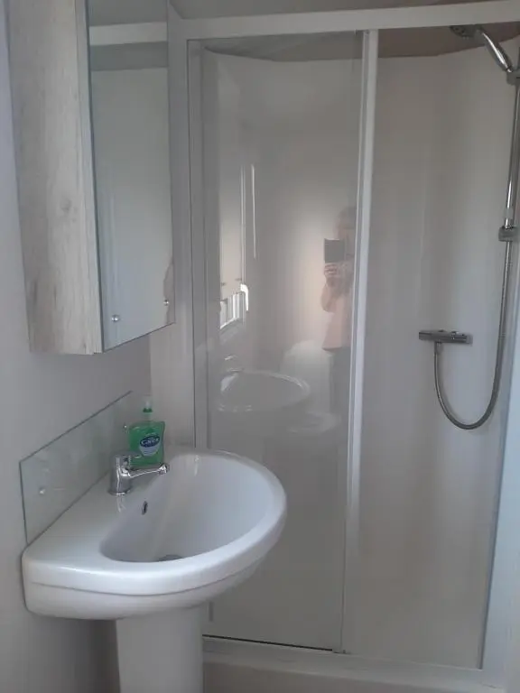 a white bathroom with a sink and a shower at Swallows at Silversands in Lossiemouth