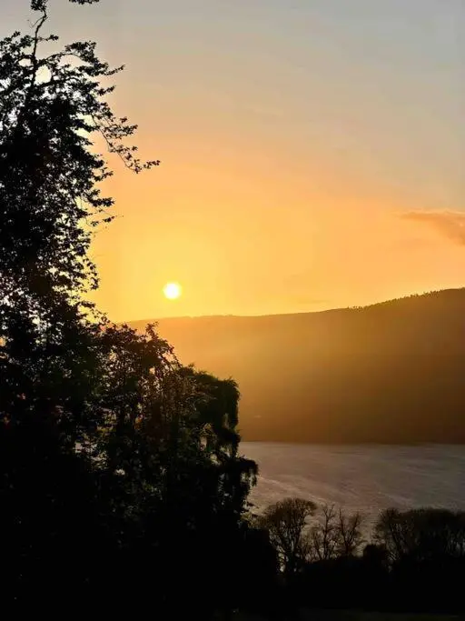 a sunset over a body of water with a tree at The Pod at Loch Ness Heights at Athbhinn, IV26TU in Inverness