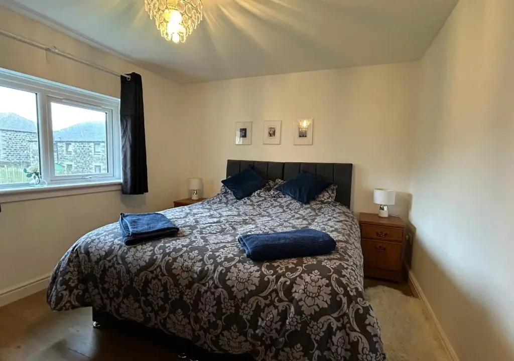 a bedroom with a bed with blue pillows on it at Carley's House, Macduff in Macduff