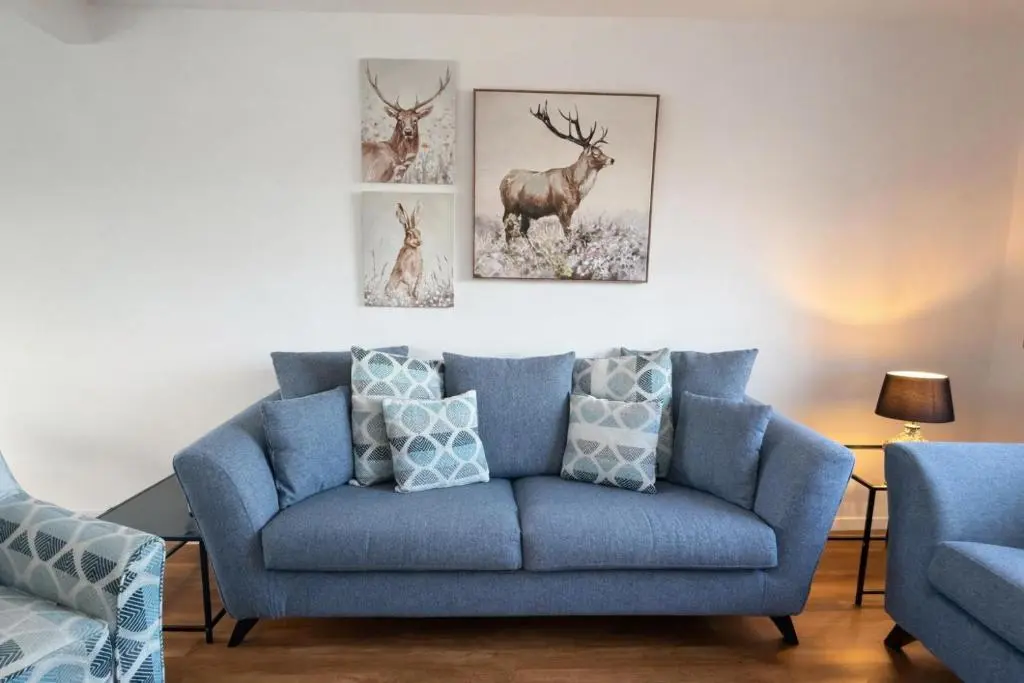 a blue couch in a living room with three deer paintings at Charlie's View in Inverness