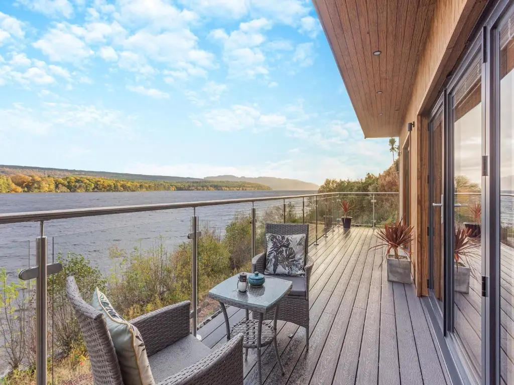 a balcony with a table and chairs and a view of the water at Kimcraigan Lodge in Lochend