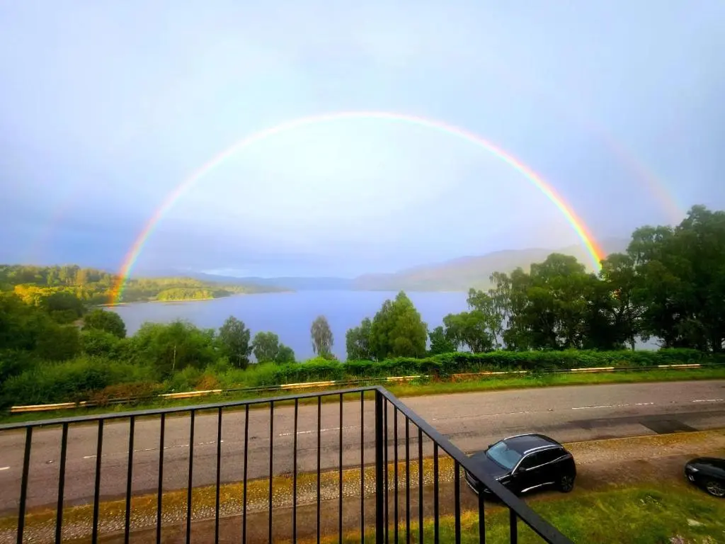 a rainbow over a lake with a car parked on the side of a road at Luichart Lodge in Lochluichart Station