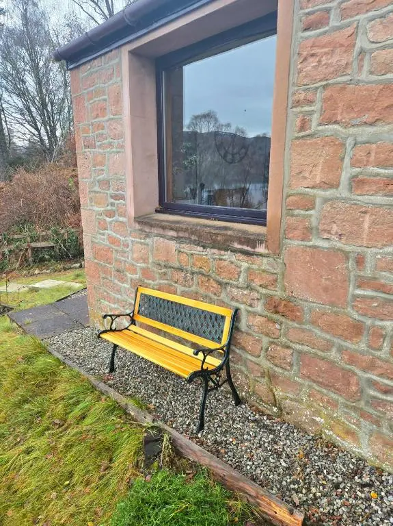 a yellow bench sitting in front of a brick building at Luichart Lodge in Lochluichart Station