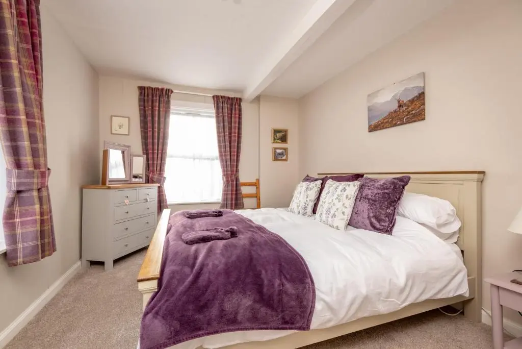 a bedroom with a bed with a purple blanket on it at Falls Cottage in Glenlivet