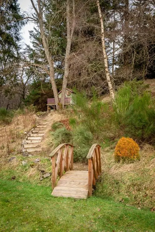a wooden bridge on a grassy hill with a bench at Falls Cottage in Glenlivet