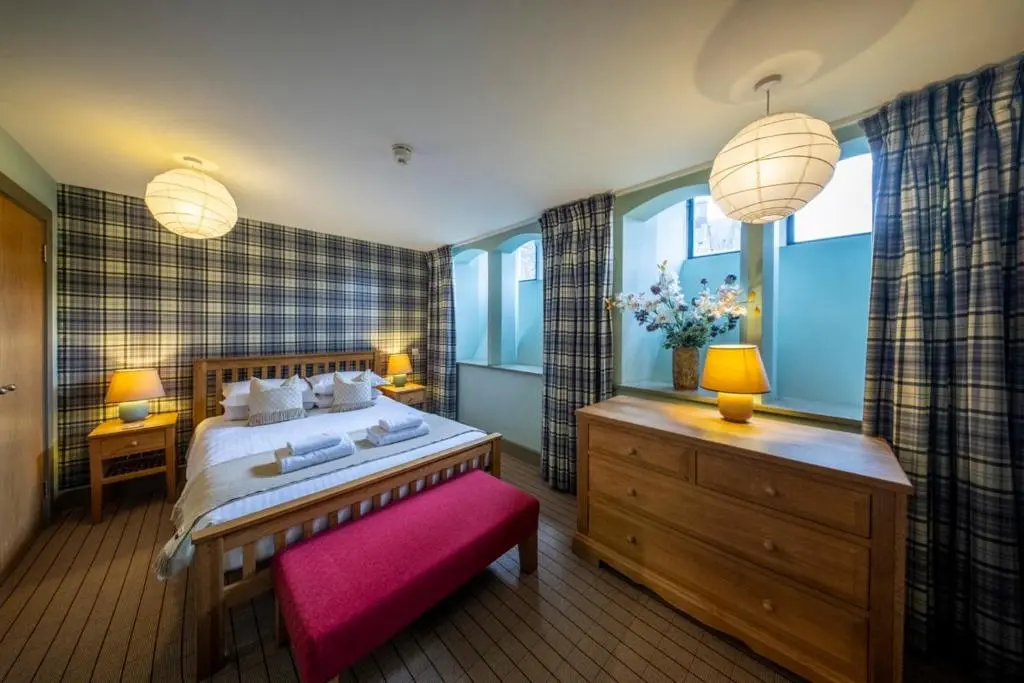 a bedroom with a large bed and a pink bench at Old School Refectory Highland Club in Fort Augustus
