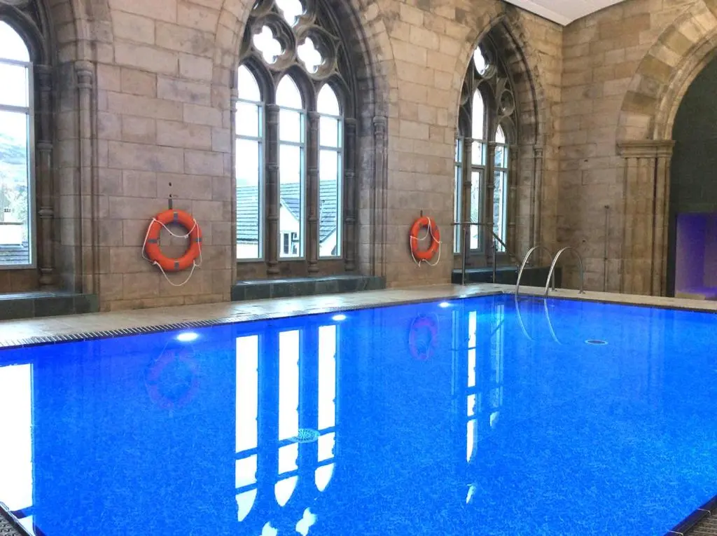 a large swimming pool with blue water in a building at Old School Refectory Highland Club in Fort Augustus
