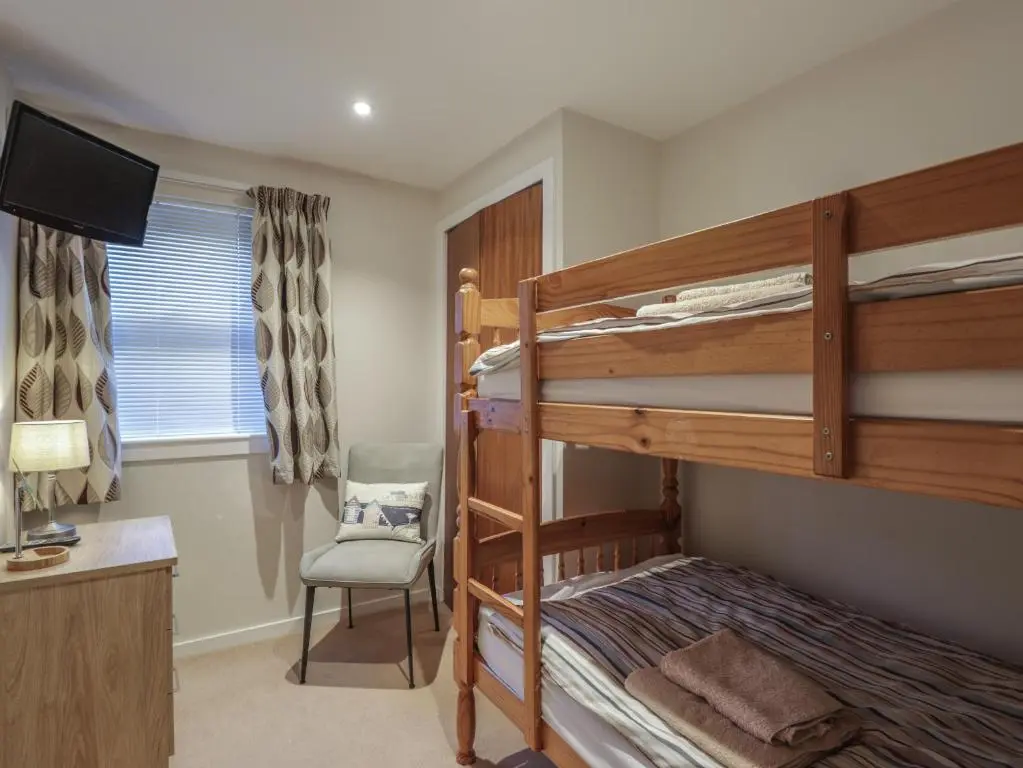 a bedroom with bunk beds with a desk and a chair at Bayside Cottage in Forres