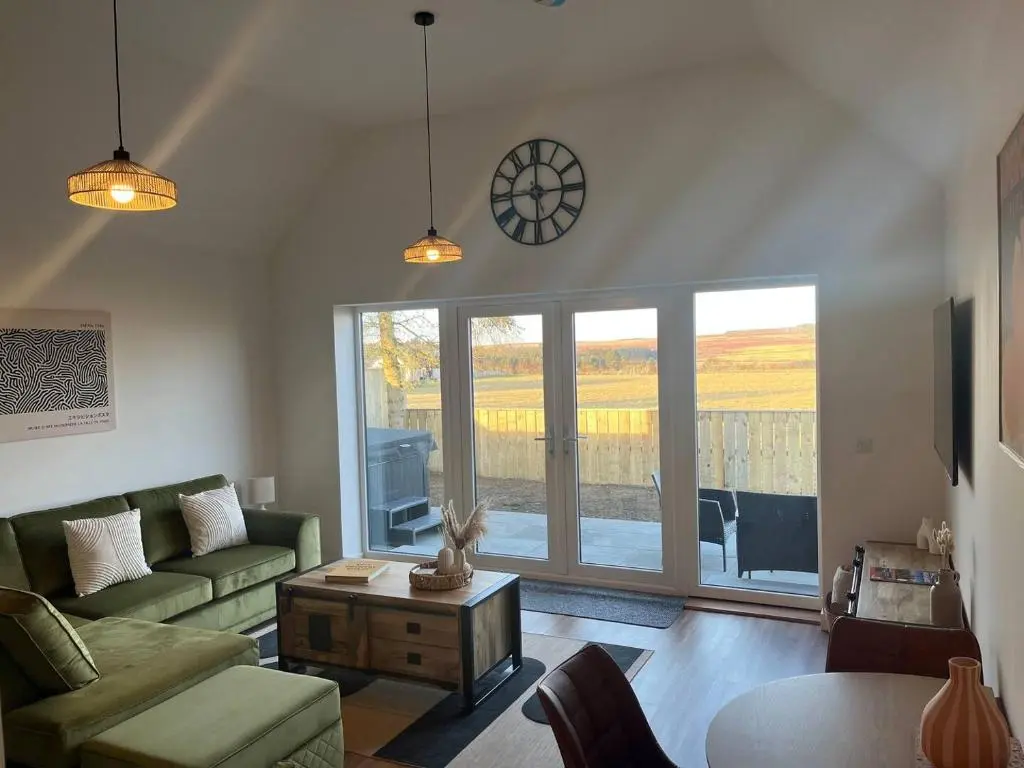 a living room with a couch and a clock on the wall at Thrumster Lodges - 3 Luxurious Self Catering Lodges on the NC500, 2 with Hot Tubs in Wick