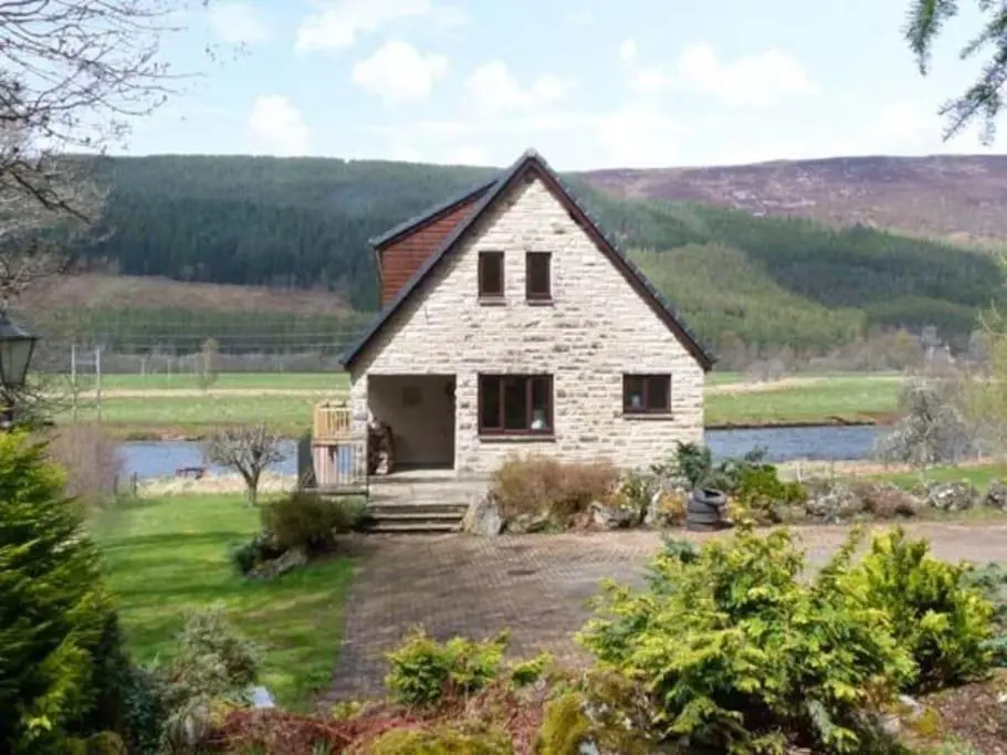 a white house in a field next to a river at Kerrow Burn Lodge Cannich Inverness-shire in Invercannich