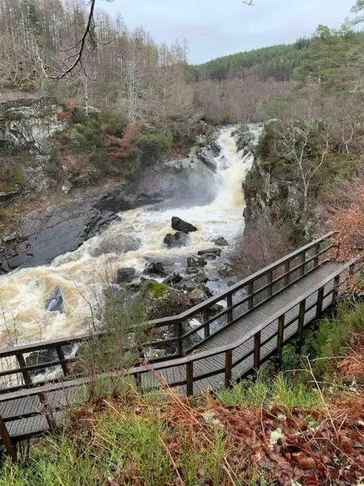 a wooden bridge over a river next to a waterfall at Bright, contemporary house & large private garden in Strathpeffer