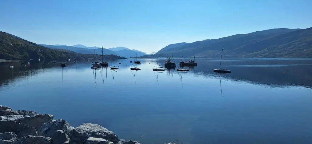a group of boats sitting on a lake with mountains at CeolMara in Ullapool