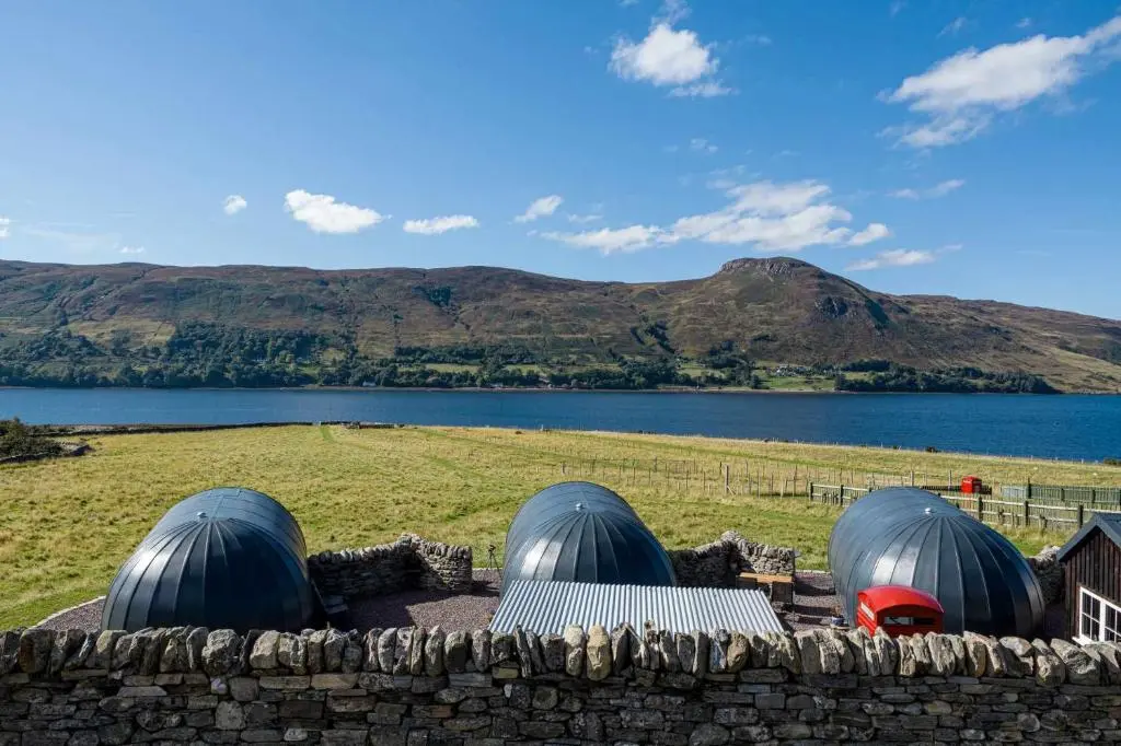 three domes on a stone wall next to a lake at Loch Broom Glamping in Garve