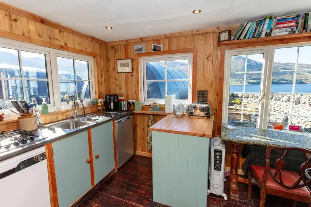 a kitchen with wooden walls and windows with a view of the ocean at Loch Broom Glamping in Garve