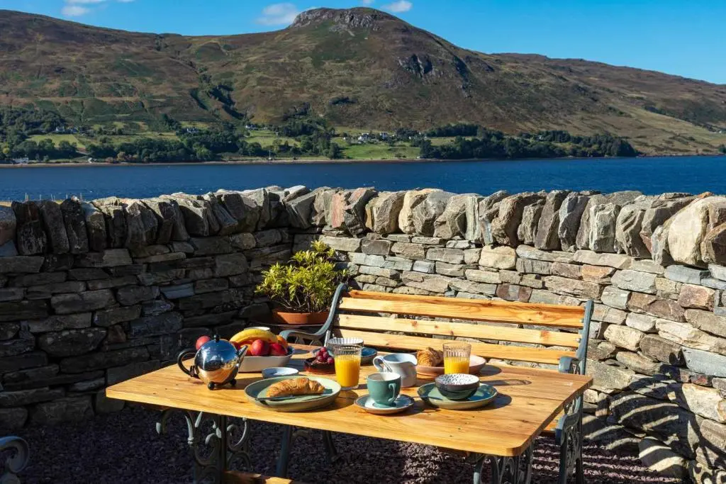 a wooden table with food on it next to a stone wall at Loch Broom Glamping in Garve
