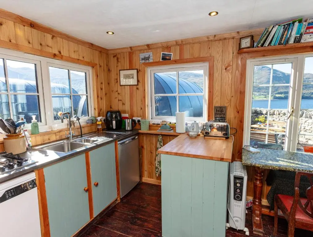 a kitchen with wooden walls and windows and a sink at Loch Broom Glamping in Garve
