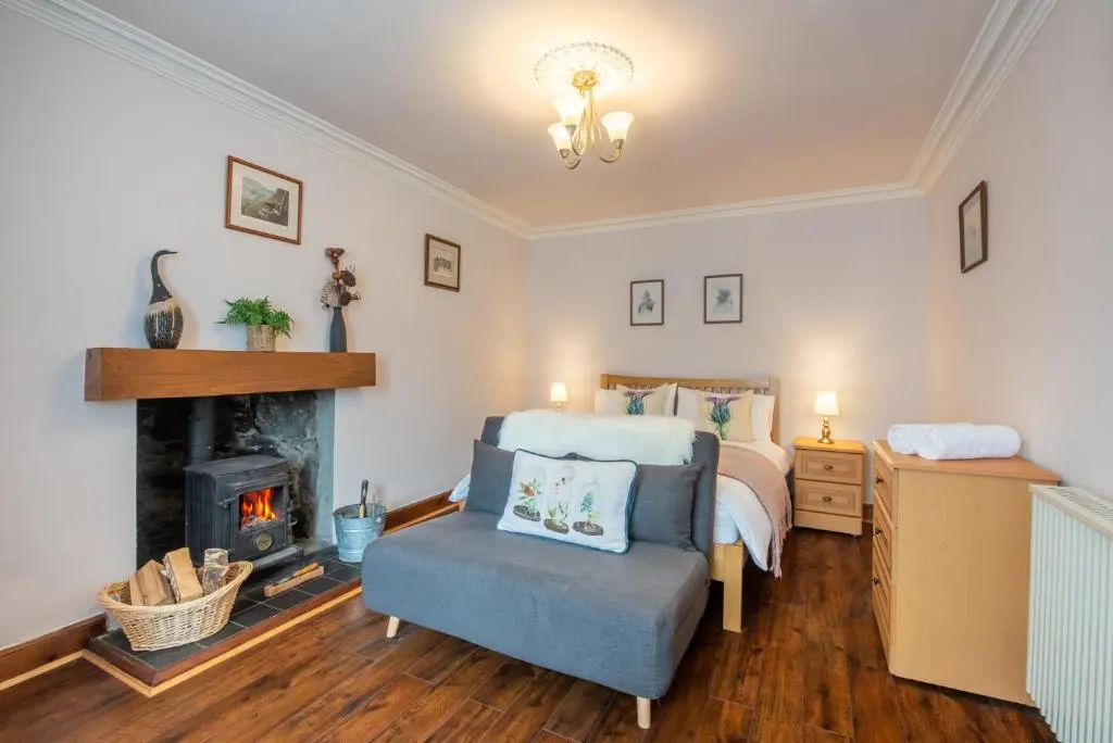 a bedroom with a fireplace and a bed and a chair at Traditional Highland Cottage Near Loch Ness in Drumnadrochit