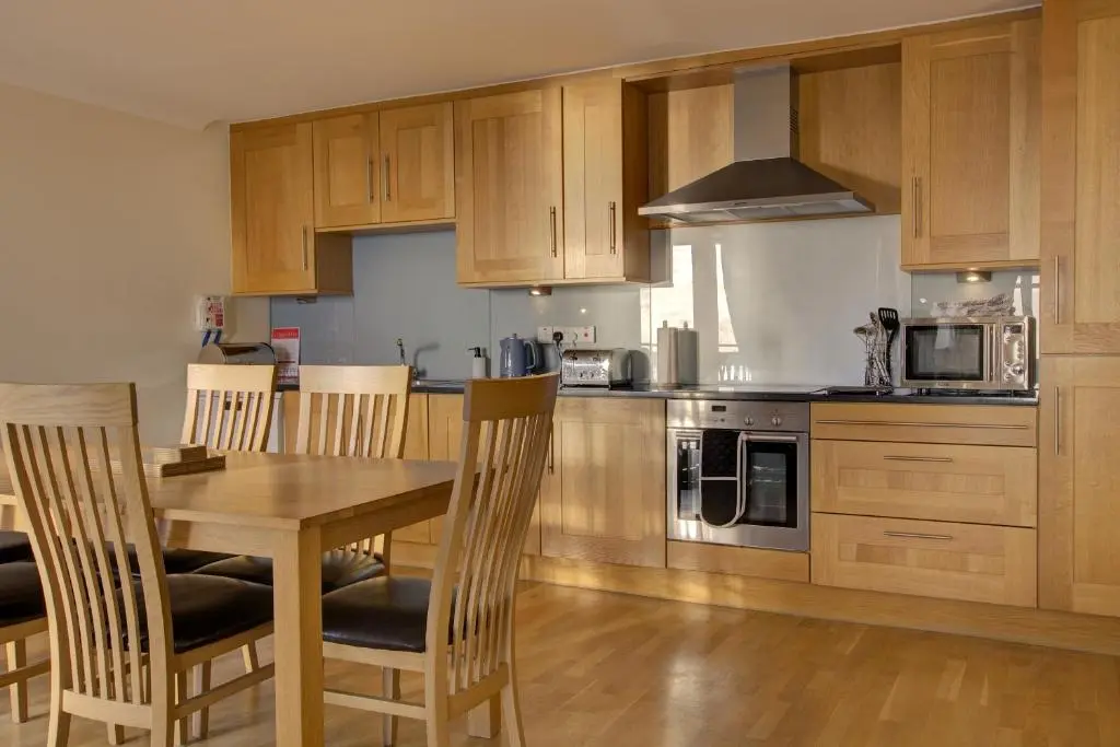 a kitchen with wooden cabinets and a wooden table and chairs at No10 The Links Apartment, Brora in Brora