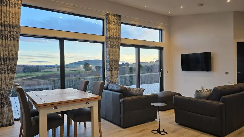 a living room with a table and a large window at Woodland Lodge in Huntly