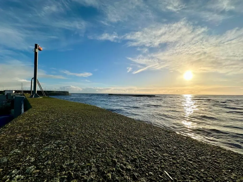 a beach with the sun setting over the water at The Old Coastguard Station in Helmsdale