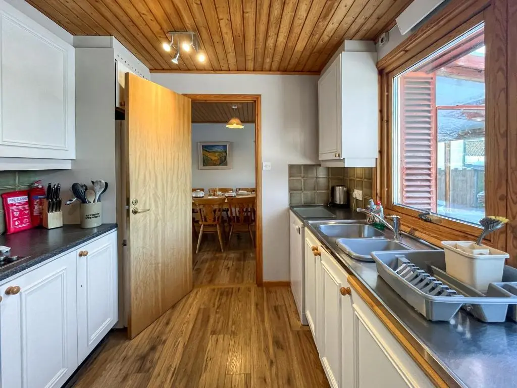 a kitchen with white cabinets and a sink and a table at Lorien Cottage in Nethy Bridge