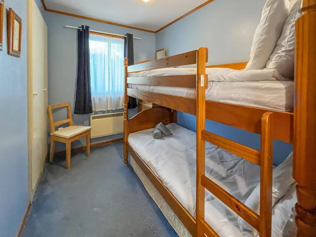 two bunk beds in a room with a chair and a window at Lorien Cottage in Nethy Bridge