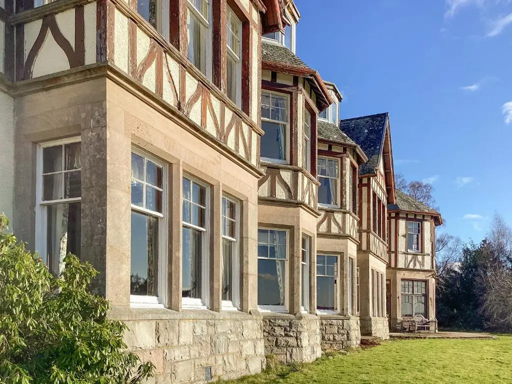 a large building with windows on a grass field at The Carnegie Rooms At Aultnagar Lodge - Uk48666 in Lairg