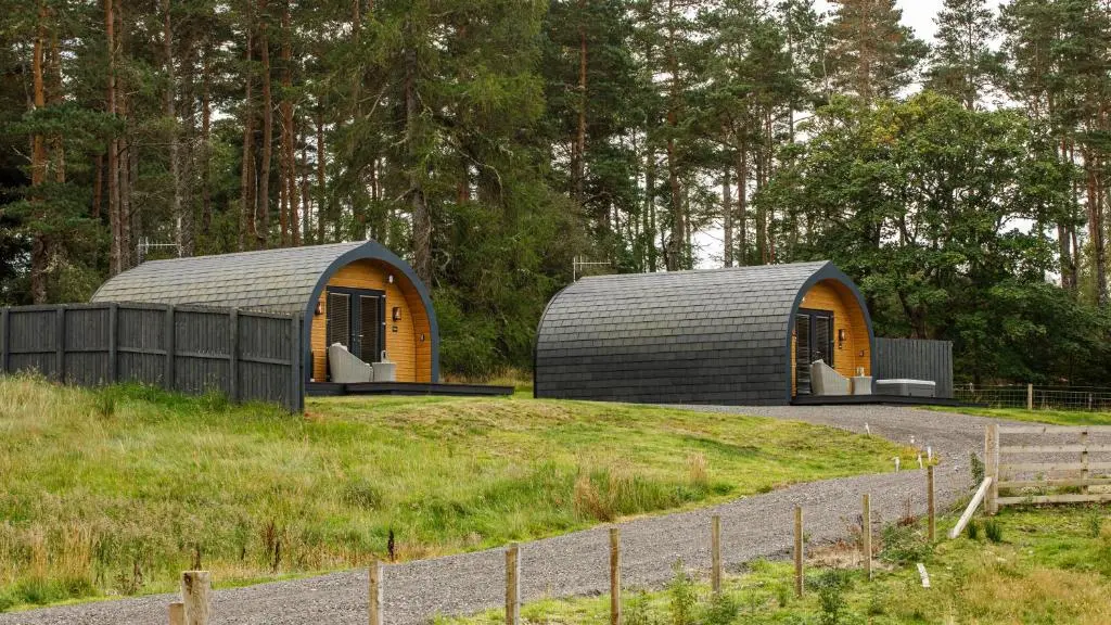 two domed buildings in a field with trees in the background at Shin View Pods in Lairg